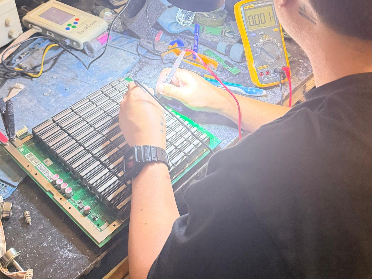 A hashboard on the bench, a hand holding a probe to it beside a multimeter