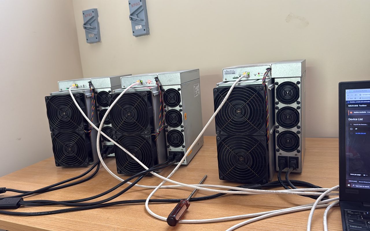 Antminer units laid out on the workshop bench beside a laptop running the test, power and network leads connected