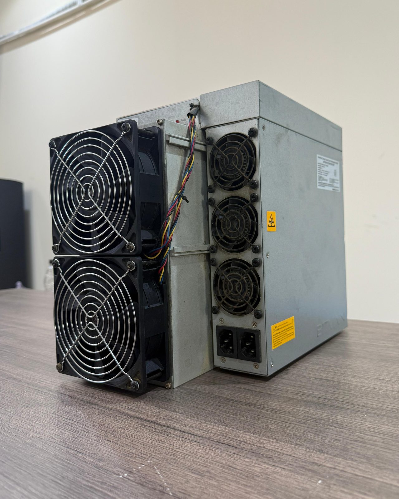 An Antminer unit standing on a wooden table, fans and power supply facing the camera